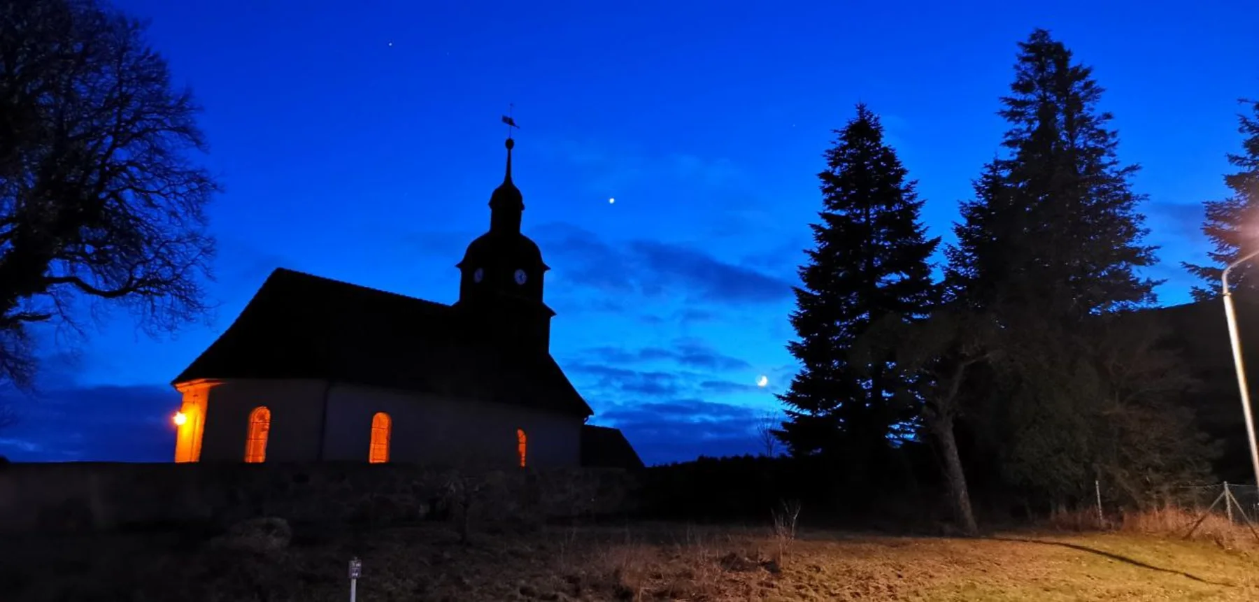 Dorfkirche Naugarten mit beleuchteten Fenstern und Mond